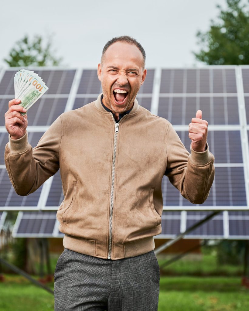 Successful investment in green energy. Man happy about money he earned by investing in alternative energy. Young male shouting cheers with money in hands.